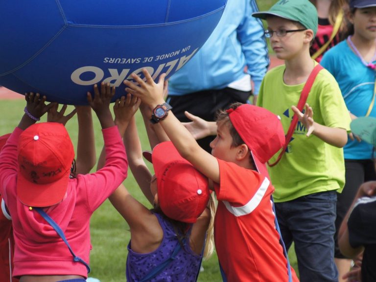 des enfants avec une casquette rouge lèvent un gros ballon bleu aux KidsGames