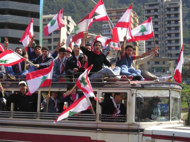 un bus avec des libanais tenant le drapeau du Cèdre à la main