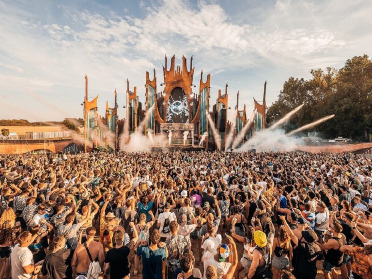 une foule de festivaliers debout devant une immense scène de musique électronique