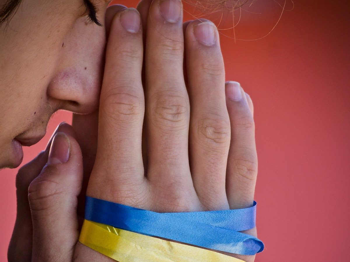 un homme prie avec des bandes bleu et jaune (Ukraine) autour des mains