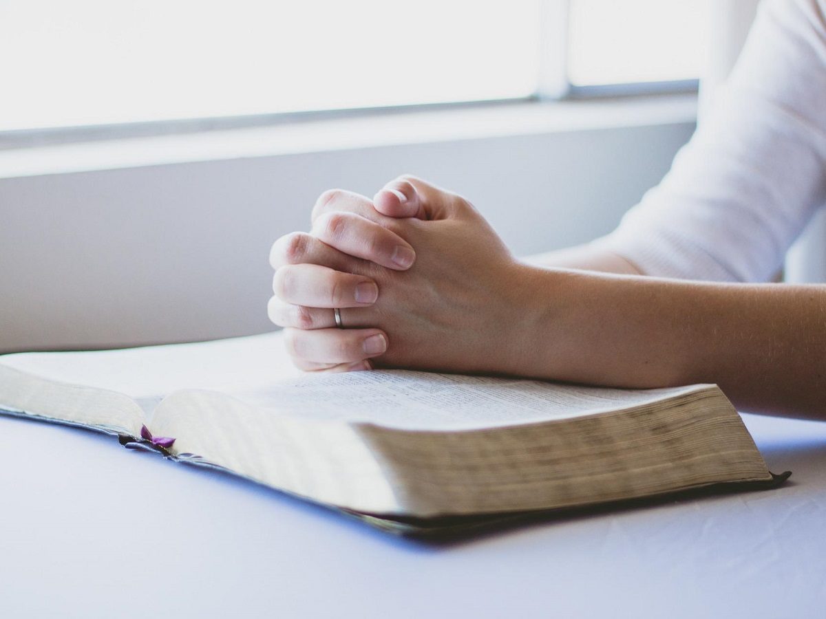une femme prie les mains croisées posées sur une Bible
