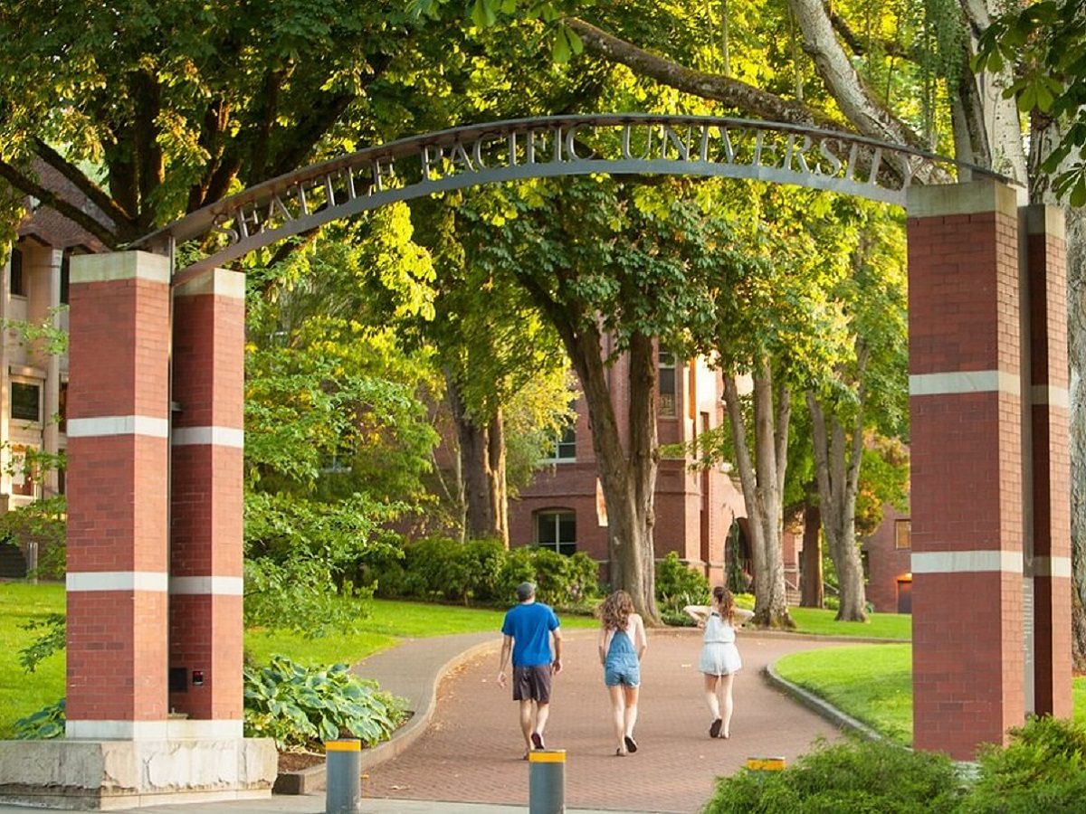 arche métallique avec des piliers en brique, trois personnes entrent dans le campus universitaire