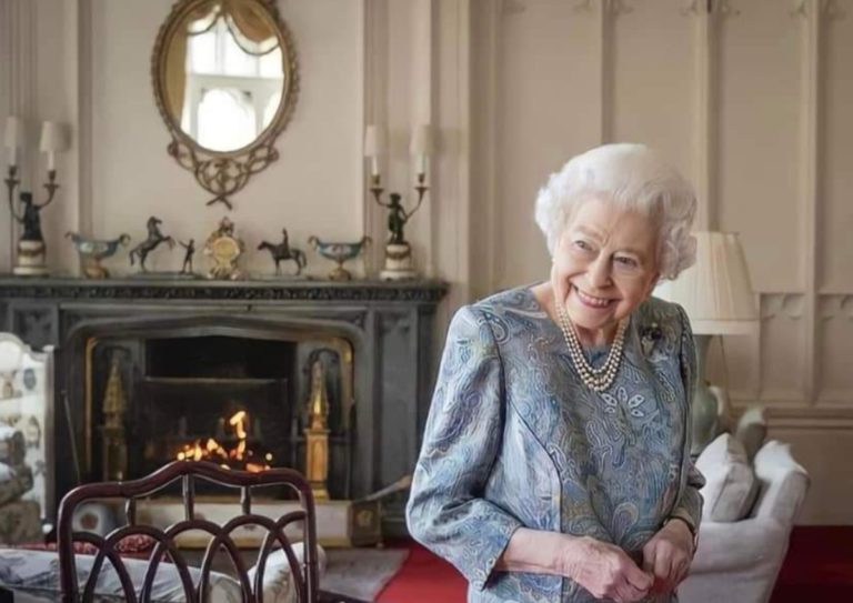 Elizabeth II en intérieur. Elle ne porte aucun ornement royal. Elle sourit à une personne qui est hors cadre.