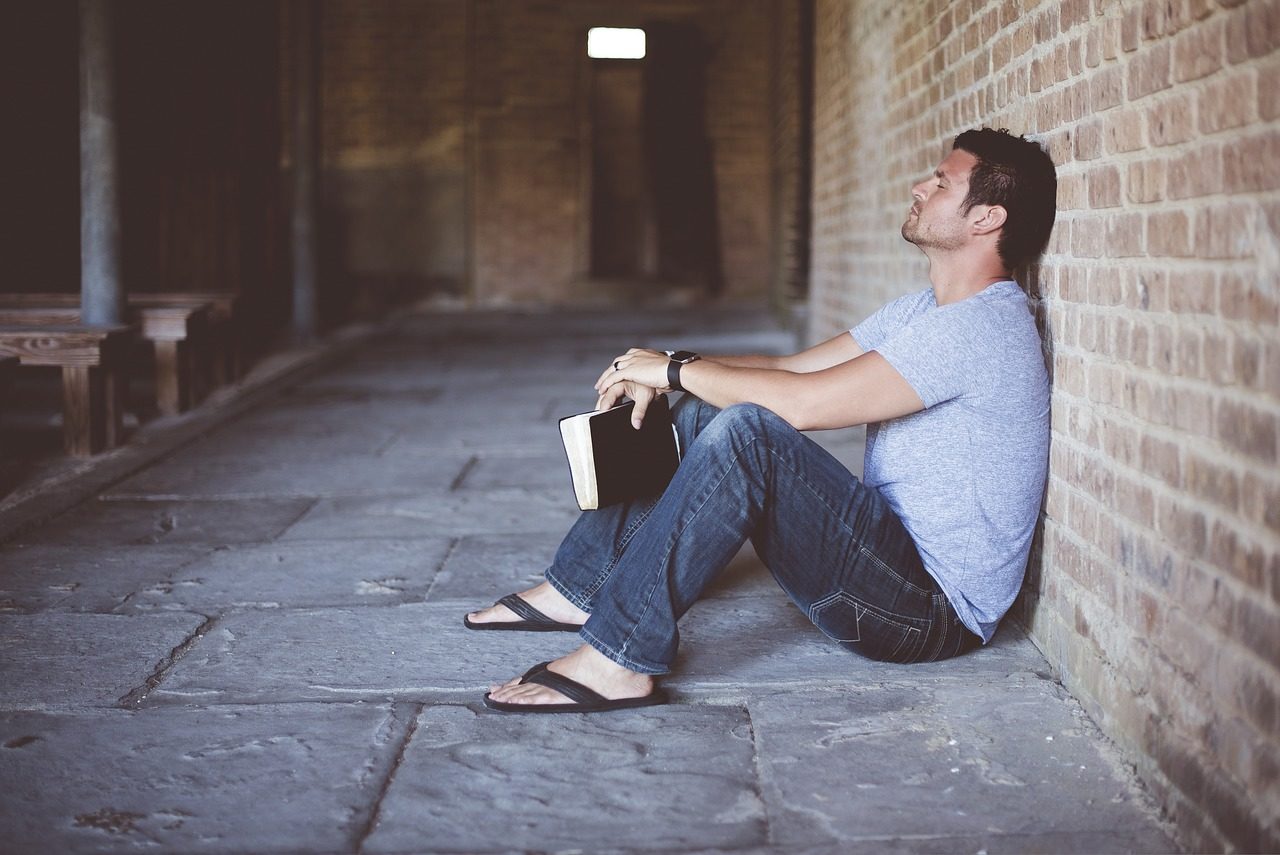 Un homme assis contre un mur réfléchit, une Bible dans la main