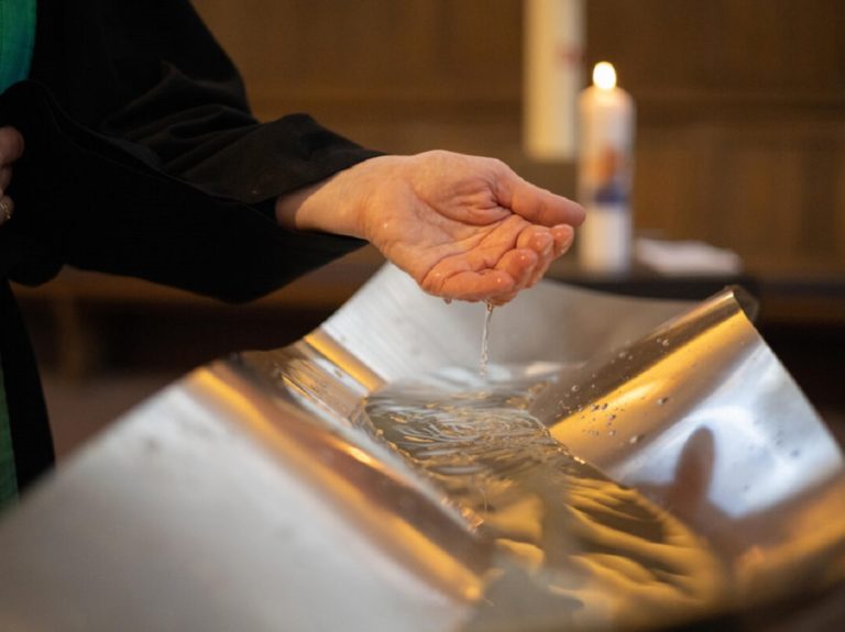 un pasteur prend de l'eau dans sa main pour baptiser