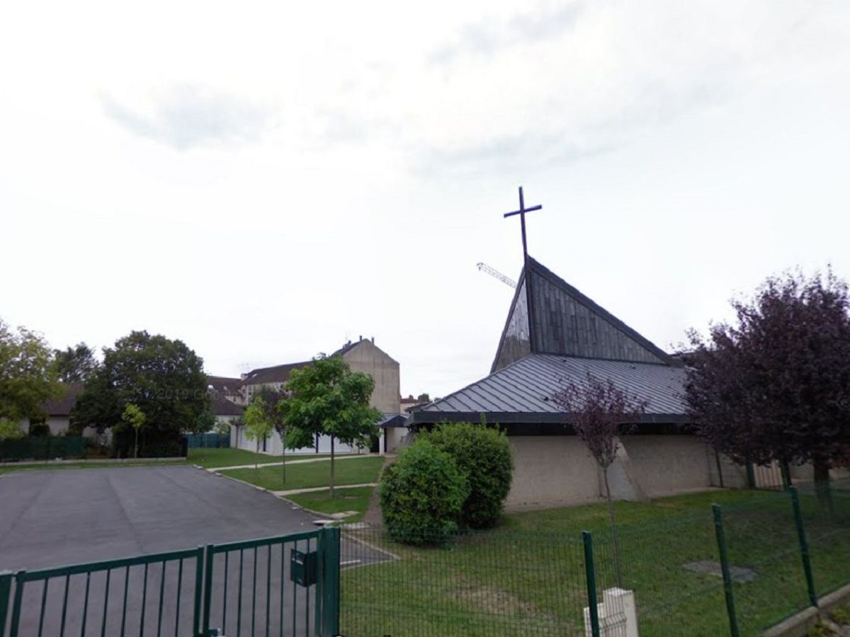 une église catholique avec une croix à son sommet entourée de végétation