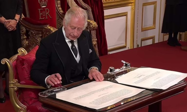Charles III signe des documents dans un bureau somptueux.