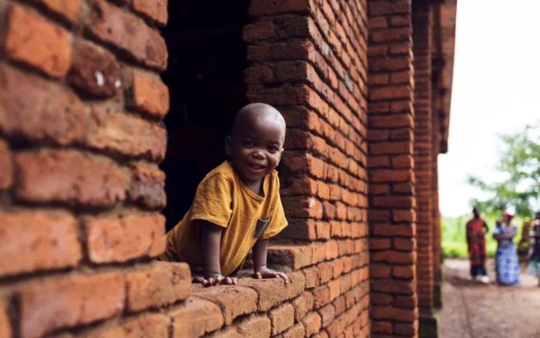 un petit enfant passe la tête par une fenêtre sans vitre aux Malawis