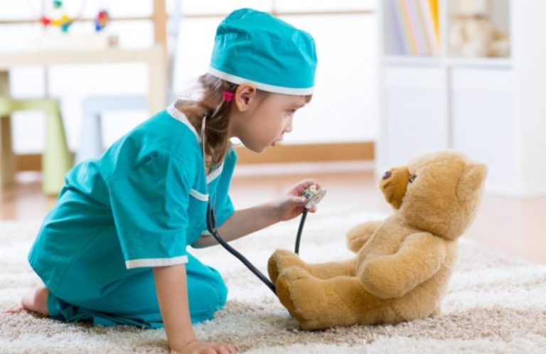 Une petite fille déguisée en chirurgien joue avec une peluche