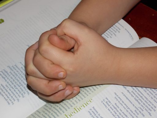 un enfant prie les mains croisées sur la Bible