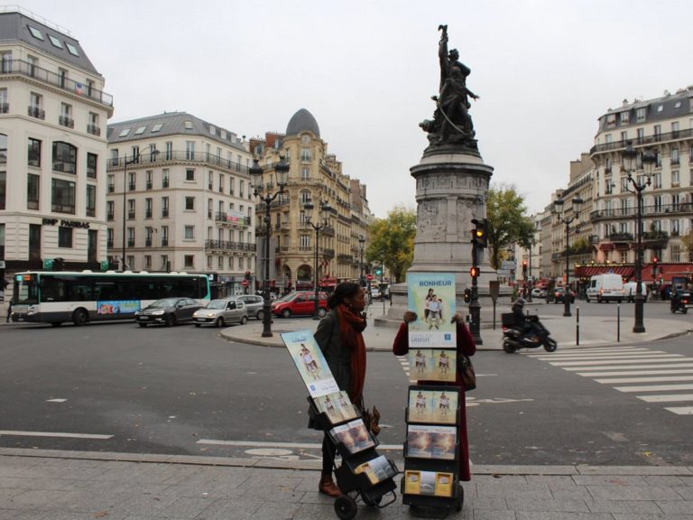 Une femme sur un trottoir de Paris avec deux chariots de prospectus des Témoins de Jéhovah