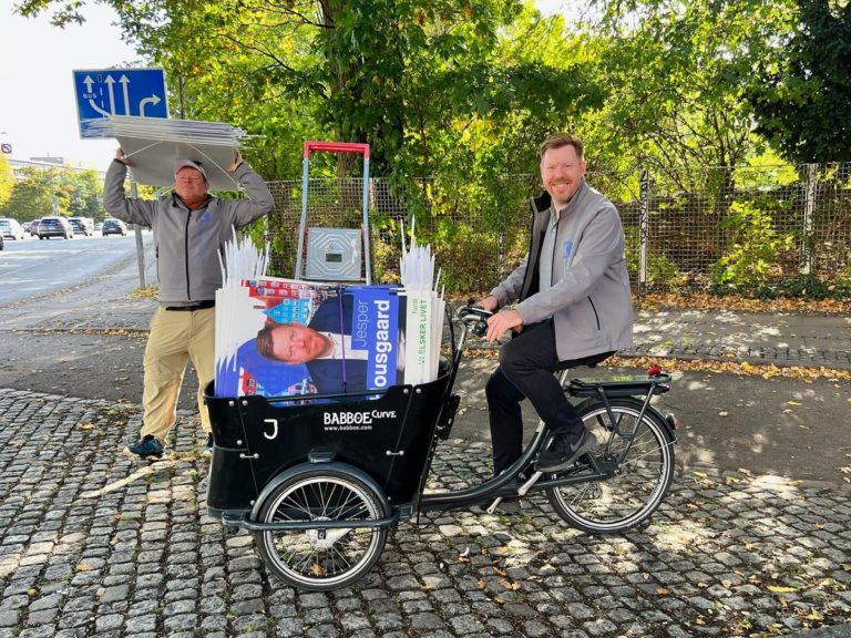 un homme politique sur un vélo avec un caddie rempli de tracts d'un candidat du parti chrétien-démocrate