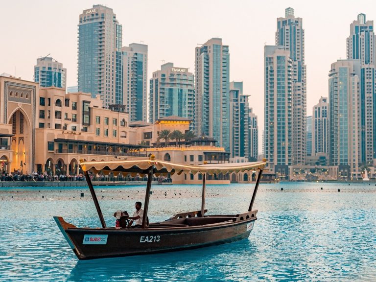 un homme aux commandes d'un bateau devant la ville de Dubaï et ses gratte-ciel au second plan