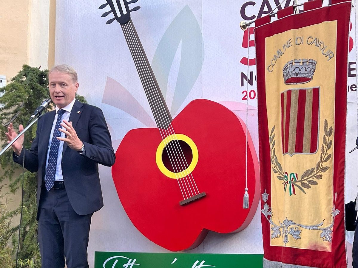 Lucio Malan s'exprime au micro, derrière lui un décor avec une guitare rouge en forme de pommes