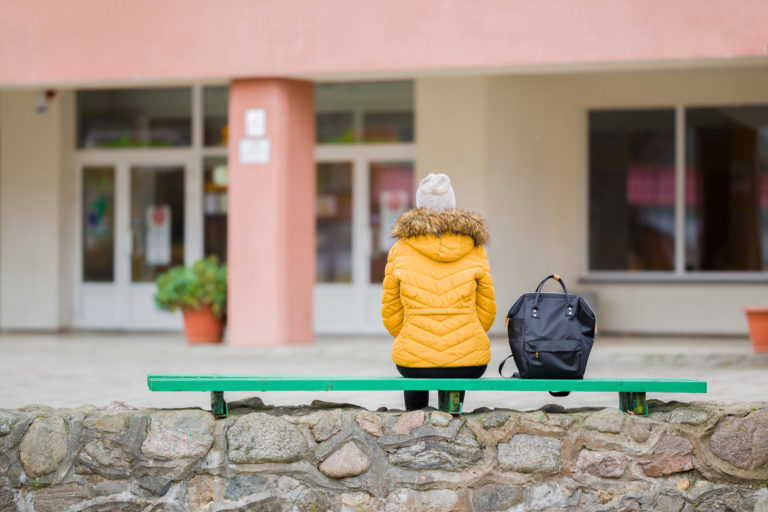 Un enfant est assis sur un banc seul devant son école