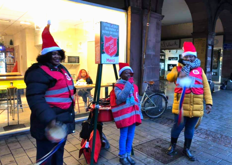 Trois personnes, dont une petite fille, tiennent le stand d'une marmite de Noël