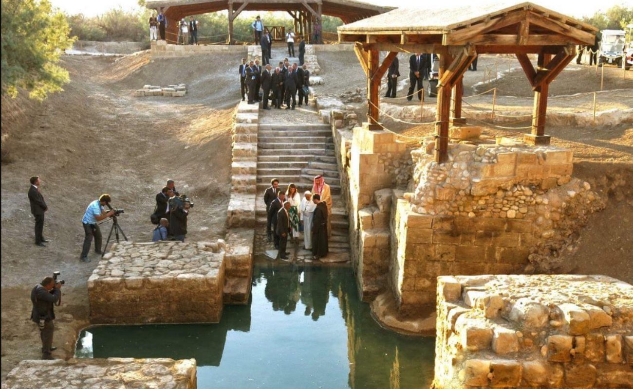 Des groupes de personnes autour d'un vieux site de baptême, dont les bords sont taillés dans la roche