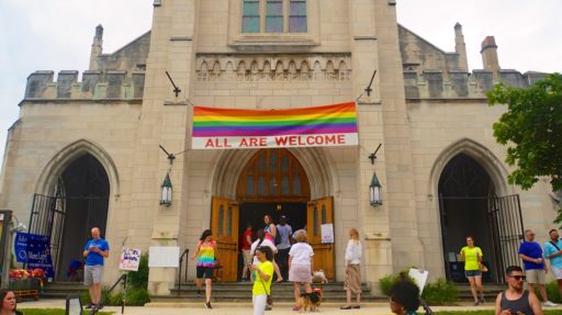 Des personnes entrent et sortent d'une église portant un drapeau LGBT