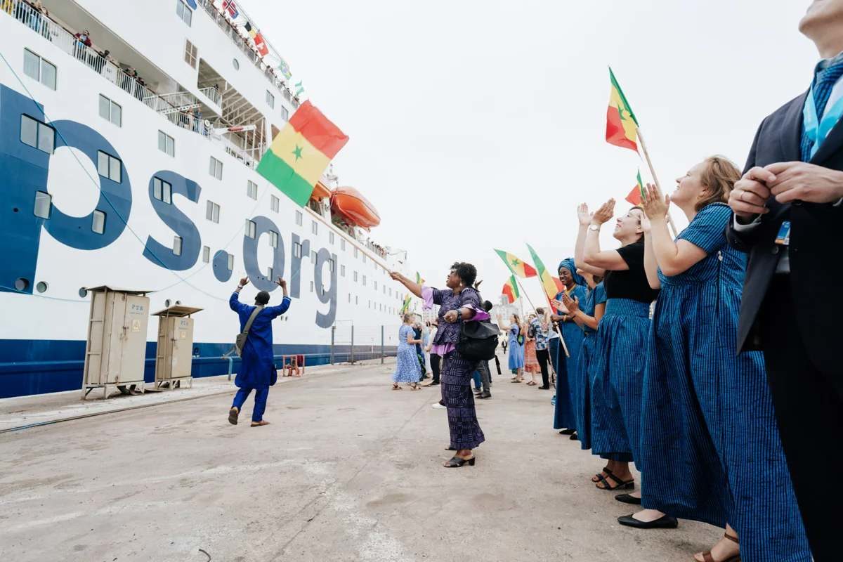 Des gens acclament avec des drapeaux sénégalais le Global Mercy arrivé à quai.