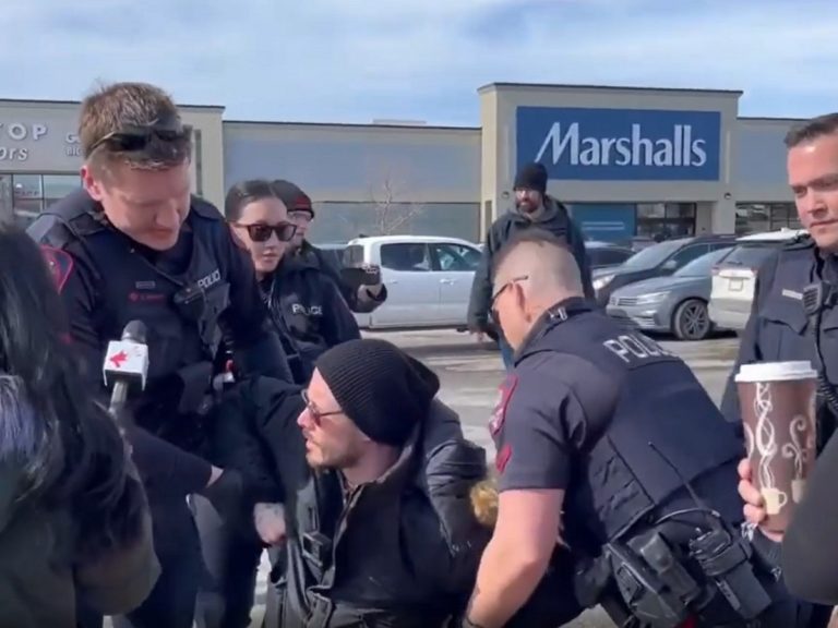 Derek Reimer menotté par la police sur les genoux sur un parking