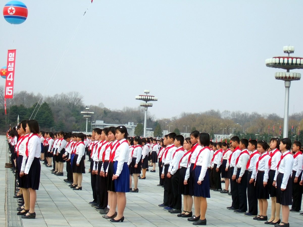 Des enfants debout sur une place avec la même tenue durant un défilé militaire