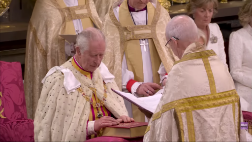 Charles III, les yeux fermés, les mains posées sur une grosse Bible, écoute l'archevêque Justin Welby.