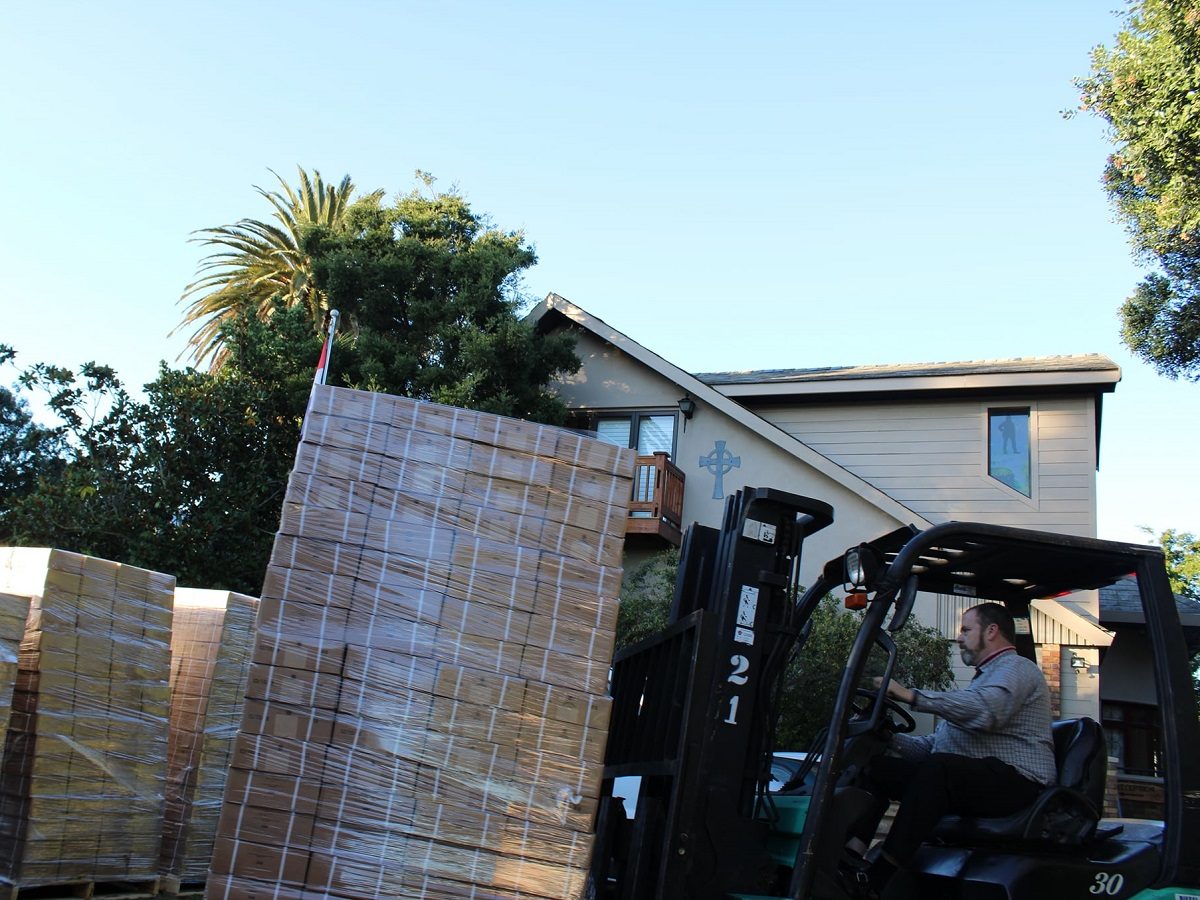 Un homme conduit un chariot élévateur qui transporte un colis de cartons emballés par un film plastique