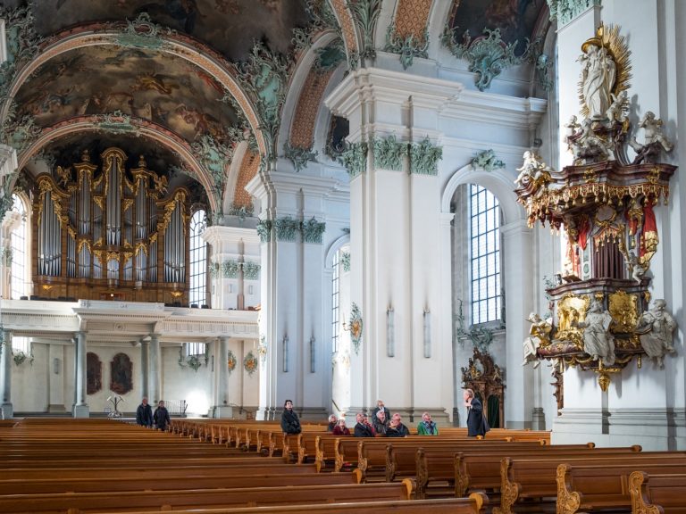 Quelques personnes assises sur les bancs d'une cathédrale regardent le plafond et ses décors