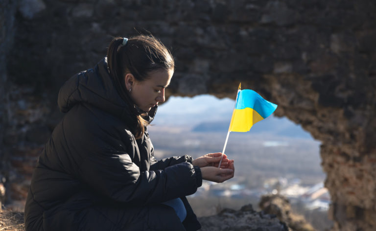 Une jeune femme assise avec le drapeau Ukrainien entre ses mains.