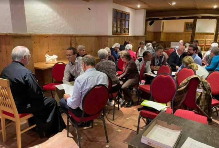 Une salle est remplie de tables où discutent des groupes de gens.