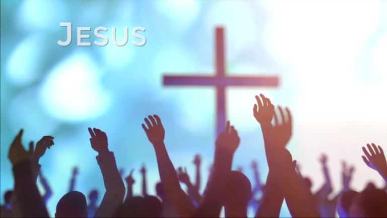 Image du clip de la chanson "Risen so we will arise". Une multitude lève les mains vers une croix qui se détache sur le ciel.