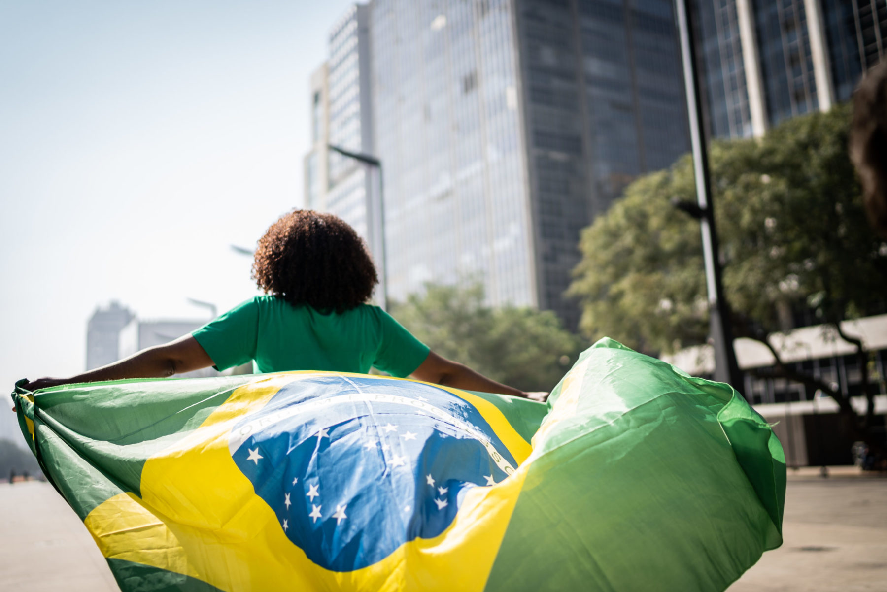 Une femme marchant de dos et tenant un drapeau brésilien