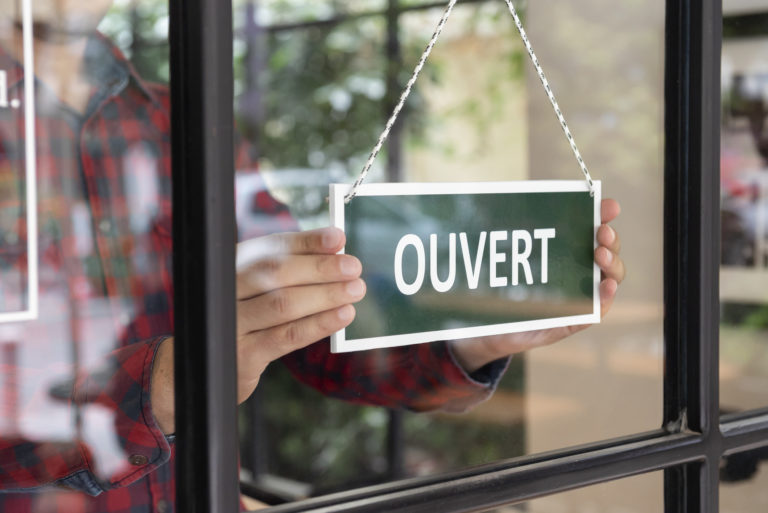 Un commerçant place un panneau "ouvert" derrière sa vitrine.