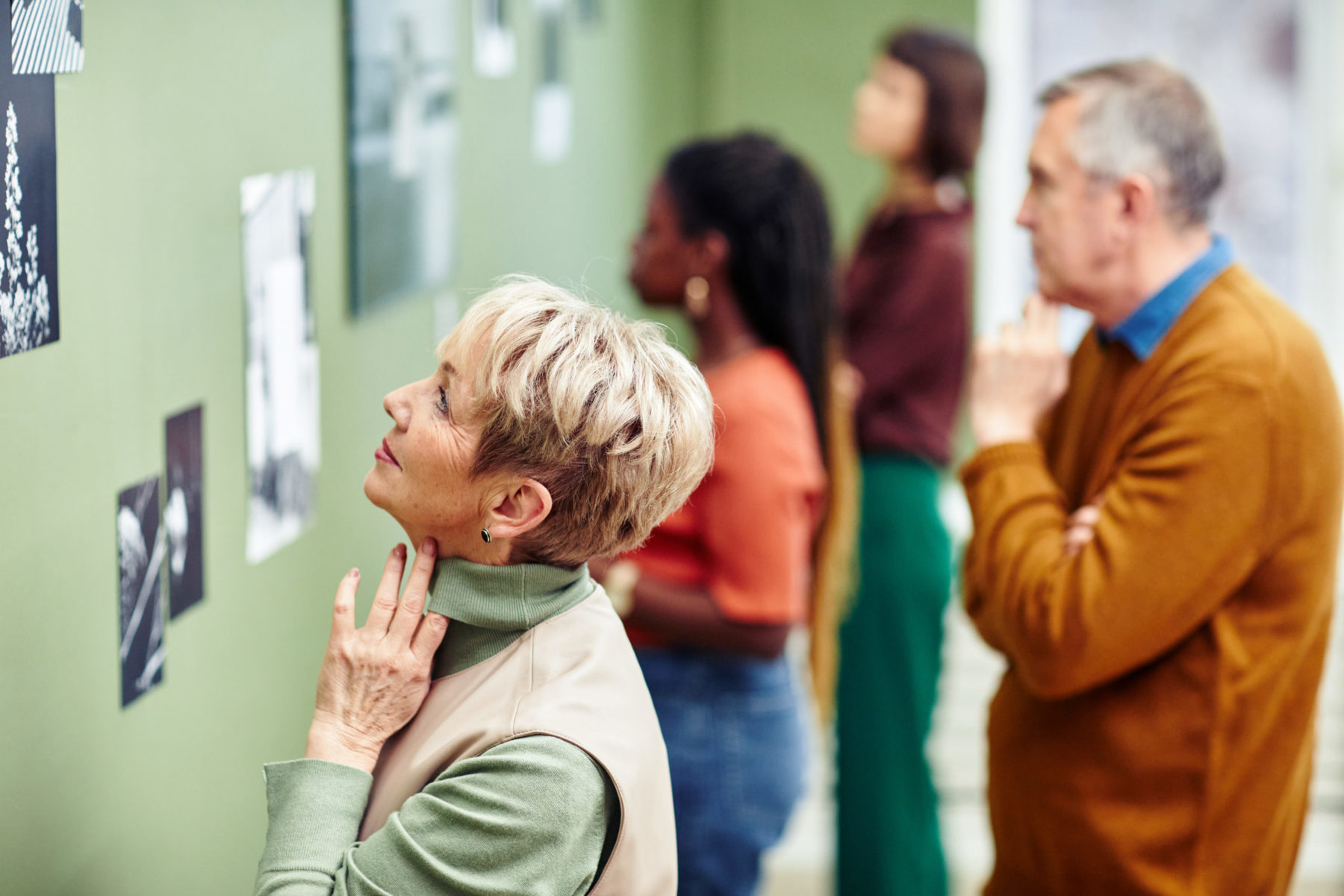 Une dame au premier plan admirant un tableau lors d'une exposition. Trois autres personnes floutées, faisant de même en arrière plan.