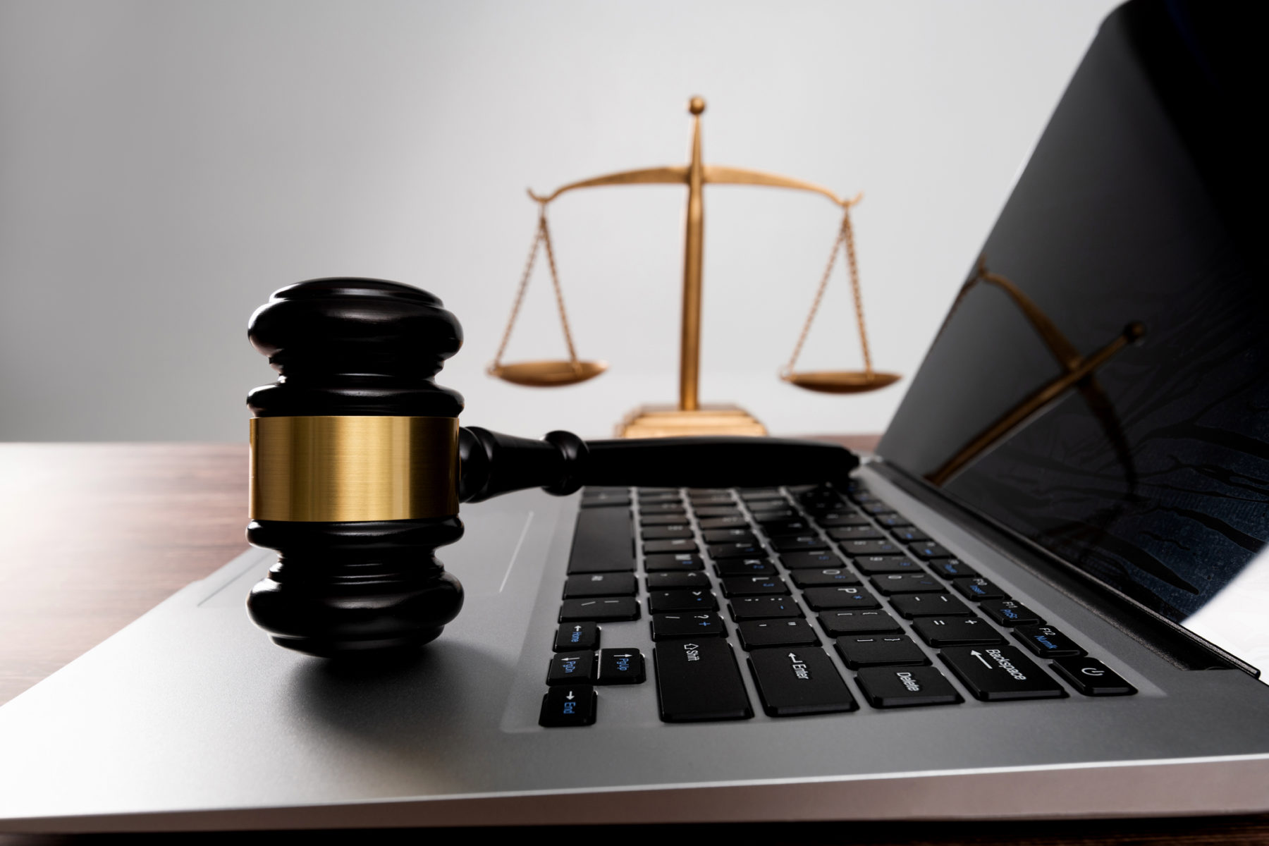 Une petite balance représentant la justice et un marteau de juge sont posés près d'un ordinateur.