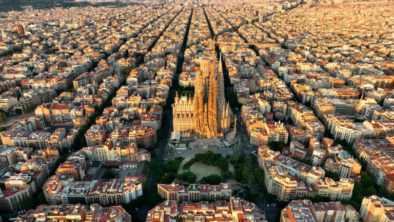 Vue d'avion sur la ville de Barcelone au coucher du soleil, la Sagrada Familia est au centre.