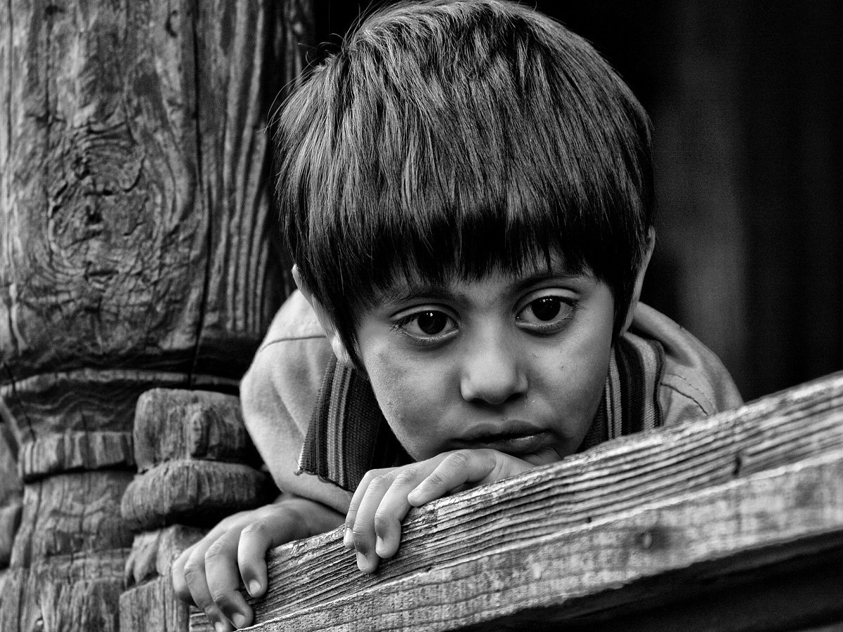 Un enfant indien a un regard triste en s'agrippant à une balustrade en bois