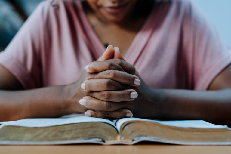 Une femme d'origine africaine a les mains croisées en prière sur une Bible