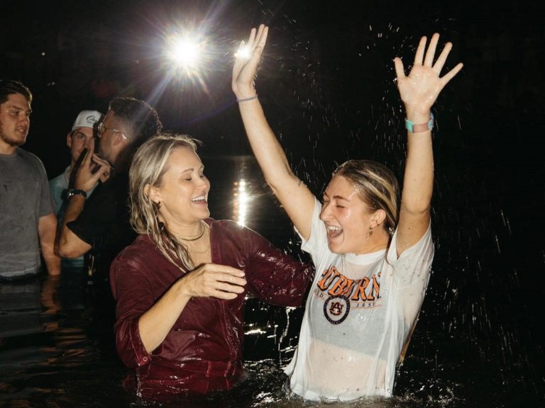 Une étudiante lève les mains dans l'eau après avoir été baptisée par une femme