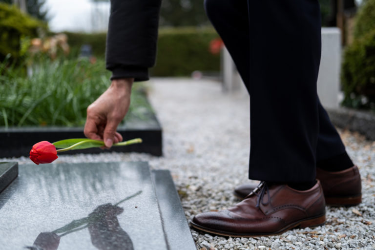 Un homme dépose une rose sur une tombe en marbre