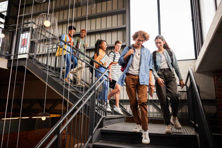 Des étudiants heureux descendent l'escalier extérieur de leur établissement