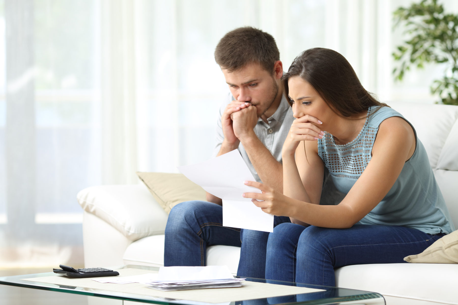 Un couple, assis sur leur canapé, regarde un document avec inquiétude