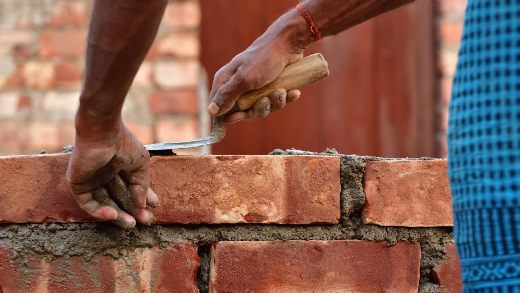 Un homme construit un mur avec des briques et du mortier