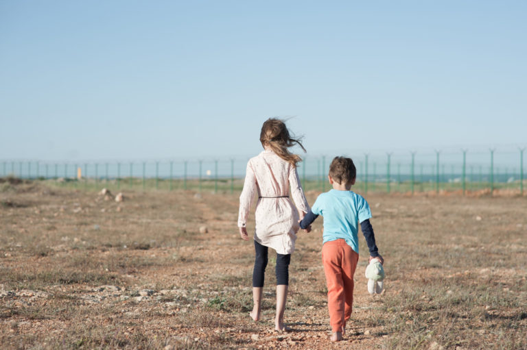 Deux enfants réfugiés marchent main dans la main en direction d'une barrière de barbelés