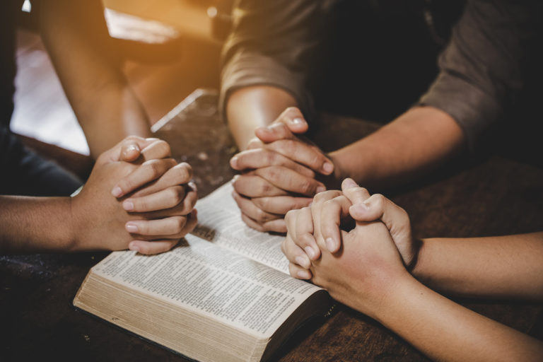 Un groupe de personne prient, les mains jointes sur une Bible