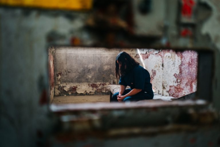 Une jeune femme est assise dans une petite cellule de prison délabrée