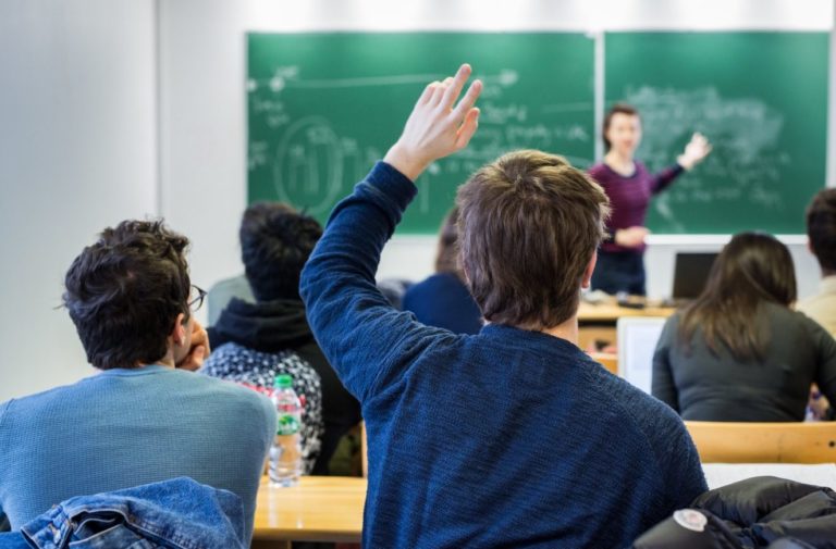 Dans une classe, un adolescent lève la main pour interpeller la professeure.