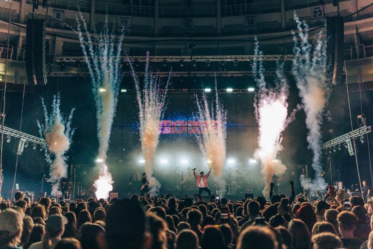 Des spectateurs debout face à une grande scène musicale avec des feux d'artifice