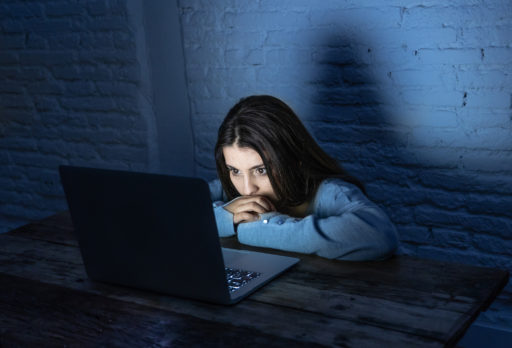 Une jeune fille fixe les yeux sur un ordinateur, la seule lumière étant celle de l'écran