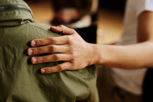La main gauche d'une personne est posé sur l'épaule droite d'une autre, le tout vu de dos